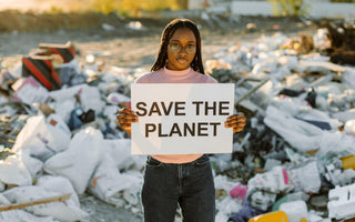 Woman environmentalist holding a sign that says "save the planet" in front of a pile of trash