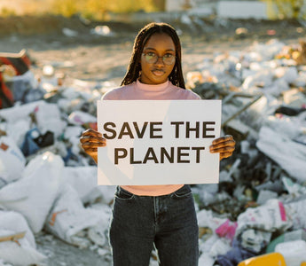 Woman environmentalist holding a sign that says "save the planet" in front of a pile of trash